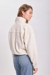 Campera de polar en color crudo, con cuello alto, cierre frontal completo y bolsillos laterales.