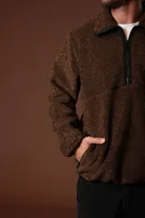 Cazadora de borreguillo color marrón, con cuello alto y cierre frontal parcial con cremallera. Presenta bolsillos laterales y diseño de manga larga.