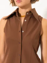 Camisa sin mangas confeccionada en tela de punto lisa, color crema, de corte regular. Lleva cartera con broches JCH y pinzas que entallan la prenda.