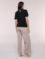 Blusa blanca de corte recto con cuello alto torzado, abertura frontal en gota y mangas cortas con aberturas sobre los hombros.