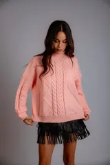 Buzo de punto color rosa con cuello alto y diseño de trenzas y rombos en relieve. Presenta mangas largas con detalle de trenzas y puños acanalados.