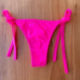 Micro tanga de lycra estampada con palmeras en tonos naranja, amarillo y rosa, con tiras laterales negras para atar.