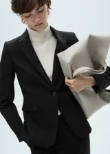 Chaqueta tipo blazer de corte entallado y diseño recto, con cuello de solapa con muesca, cierre frontal de un botón, hombros estructurados y manga larga con puños abotonados. Cuenta con dos bolsillos de ribete delanteros y un bolsillo de ribete en el pecho, además de una abertura posterior.