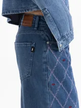 Jeans de denim azul, tiro medio y corte recto, con bordado integral en patrón de rombos en hilo rosa y pequeños bordados de labios en color bordeaux.