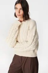 Sweater de punto color crudo con cuello alto y mangas largas abullonadas. Presenta apliques de cuero marrón en forma de rombos en los codos.