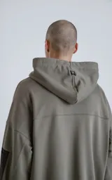 Hoodie oversize color verde militar, confeccionado en algodón rústico. Presenta capucha forrada, bolsillo frontal tipo canguro y un bolsillo adicional con cierre en la manga izquierda, con detalles en microfibra negra.