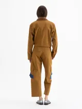 Pantalón de gabardina color marrón, de tiro alto y silueta estructurada. Cuenta con volados de denim azul aplicados sobre los bolsillos plaqué laterales y bolsillos plaqué traseros con remache dorado.