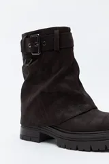 Bota de caña media color negro, con suela robusta dentada y detalle de hebilla ajustable en la parte superior. Presenta una argolla metálica lateral y un diseño de estética urbana con acabado texturizado.