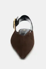 Zapato plano destalonado de ante color marrón oscuro, con punta fina y tira trasera ajustable con hebilla metálica dorada.