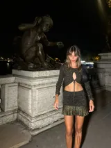 Top corto de tejido de punto negro con hilos dorados, manga larga con orificio para el pulgar, abertura en el pecho y cordones para cerrar el frente.