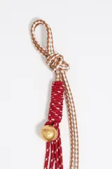 Colgante para bolso con cordones de cuero marrón, cordones trenzados naranja y verde, y dije metálico plateado.