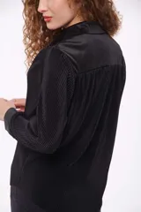 Camisa negra de poliéster con textura plisada, corte recto, cuello camisero y cierre frontal con botones.