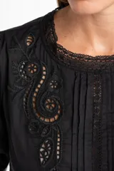 Blusa negra de algodón con corte oversize, mangas cortas abullonadas y detalles de encaje y bordados en el frente y hombros. Presenta un diseño con pliegues verticales y terminaciones con puntilla.