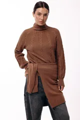 Polera de tejido de punto color marrón, con cuello alto y diseño de trenzas verticales. Presenta mangas largas con puños ajustados y un detalle de panel lateral asimétrico que se anuda en la cintura.