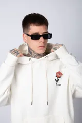 Buzo tipo canguro de corte oversize, color blanco, con capucha y cordones ajustables. Presenta un pequeño estampado de una rosa roja en el pecho y un bolsillo frontal tipo canguro.