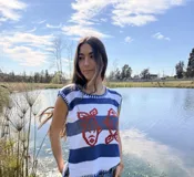 Chaleco tejido de algodón color crudo, con escote redondo y detalles de ribetes azules. Presenta un estampado frontal de dos peces en color azul marino.