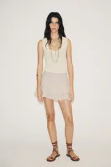 Falda pantalón corta color beige claro, de tiro medio, con efecto drapeado en la cintura y volantes superpuestos en el ruedo.