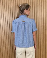 Camisa de manga corta color beige, con cuello alto con volados, botonadura frontal y mangas abullonadas con terminación fruncida.