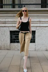 Bermuda larga de tiro medio color beige, con bolsillos en el delantero, pinzas y cierre frontal con cremallera y ganchos metálicos. Incluye cinturón fino de cuero sintético negro con hebilla metálica.