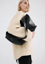 Bolso tipo hobo color negro, confeccionado en poliuretano con textura granulada, asa de hombro integrada y diseño amplio y flexible.