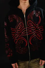 Hoodie con cierre frontal completo, confeccionado en algodón de tejido grueso. Presenta un diseño estampado en serigrafía con motivos de hojas de acanto en color rojo sobre fondo negro. Cuenta con bolsillos laterales y cierre metálico YKK.