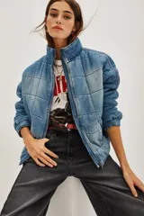 Campera acolchada de denim con efecto lavado, cuello alto y cierre frontal. Presenta un diseño de costuras cuadradas y mangas largas con puños elásticos.