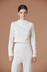 Blusa de manga larga con cuello alto y textura plisada con ondas verticales. Presenta un corte cropped y detalles de botones dorados en los puños.