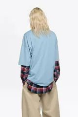 Remera de corte oversize color celeste con cuello redondo y mangas cortas. Presenta un estampado frontal con el logo de la marca y un dibujo de zapatillas de ballet en color rojo.