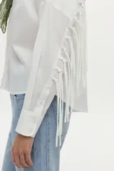 Camisa blanca de manga larga con flecos en la espalda y las mangas, confeccionada en mezcla de algodón, poliamida y elastano.