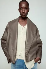 Cazadora Zara Woman Collection de efecto piel con cuello solapa ancho, manga larga, bolsillos delanteros y bajo elástico. Presenta un cierre frontal cruzado con botón a presión.