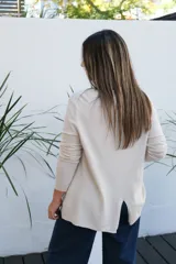 Sweater de tejido de punto en color beige, con cuello redondo, mangas tres cuartos y corte holgado con ruedo ligeramente más largo en la parte posterior.