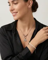 Set de joyería en acero compuesto por un collar con dije circular de trébol de cuatro hojas y un par de aros tipo bolita. El collar presenta una cadena con esferas decorativas en la parte central.