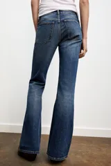 Jeans de tiro bajo con diseño bootcut, cinco bolsillos y trabillas para cinturón. Presenta un acabado flare en el bajo y cierre frontal con cremallera y botón metálico.