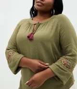 Blusa de viscosa color verde oliva, con cuello redondo, lazo con borlas decorativas y mangas largas con bordado étnico en los puños.