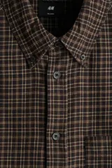 Camisa de sarga de algodón marrón con estampa de cuadros, cuello americano, cierre frontal de botones, manga larga con puños abotonados y bolsillo en el pecho.