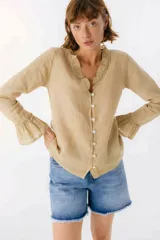 Blusa de lino color beige con volados en el escote y en los puños de las mangas largas. Cierre frontal con botones de nácar.