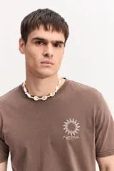 Remera de algodón marrón con efecto lavado, cuello redondo y manga corta. Cuenta con un pequeño estampado frontal de un sol estilizado y la inscripción "Mistral".