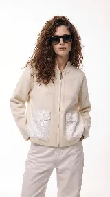 Campera de corte relajado color crema, con cierre frontal completo y cuello tipo bomber. Presenta dos bolsillos frontales destacados con apliques de lentejuelas blancas.