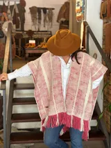 Ruana de lana merino tejida en telar, con diseño de rayas verticales en tonos crudo y rojizo, y terminación de flecos en el ruedo.