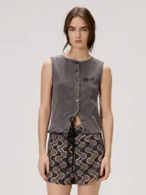 Musculosa MUTMA modelo Trebola de silueta recta, confeccionada en tejido de punto gris tipo lavado. Cuenta con cierre frontal de botones, bordado pequeño en el pecho y terminación festoneada en el ruedo y sisas.