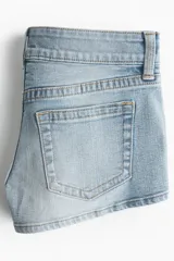 Minishorts de cinco bolsillos en denim levemente elástico de color celeste, con corte ajustado, tiro bajo y cierre con botones. Cuenta con un bolsillo monedero con solapa y botón.