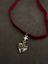 Gargantilla tipo choker con cinta de terciopelo rojo y dije metálico en forma de Sagrado Corazón con cruz superior.