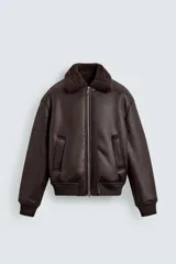 Cazadora oversize de efecto piel color marrón oscuro, con interior y cuello de corderito sintético a tono. Posee cierre frontal de cremallera metálica, bolsillos ribeteados en la cadera y puños y dobladillo de rib elástico.
