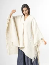 Ruana off white de tejido texturado con detalles sutiles de hilos multicolor y terminación de flecos en los bordes.