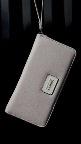 Billetera larga con cierre perimetral, confeccionada en material sintético texturizado color mostaza. Cuenta con correa de mano extraíble y placa metálica con logo de la marca en el frente.