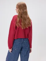 Cardigan de algodón grueso color rojo, con cuello redondo, cierre frontal de botones grandes y bolsillos cuadrados en el frente. Presenta detalles de pelo sintético en el cuello y los bolsillos, y logo bordado en uno de los bolsillos.