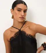 Vestido negro de satén con escote halter y tirantes finos ajustables. Presenta un bajo asimétrico con acabado de encaje.