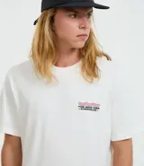 Remera de algodón color blanco, corte comfort, con cuello redondo y manga corta. Presenta un pequeño estampado en el pecho con tres líneas onduladas rojas y negras, y texto debajo.