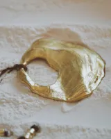 Collar artesanal con dije de bronce macizo en forma orgánica irregular, similar a una concha marina, suspendido de un cordón de seda natural negro. El diseño permite diversas formas de uso, ya sea ajustado al cuello o largo.