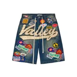 Short de denim azul con calce baggy, gran aplicación bordada con la inscripción "Valley" decorada con tachas y brillos, además de múltiples parches coloridos bordados por toda la prenda y cordones largos colgando de la cintura.